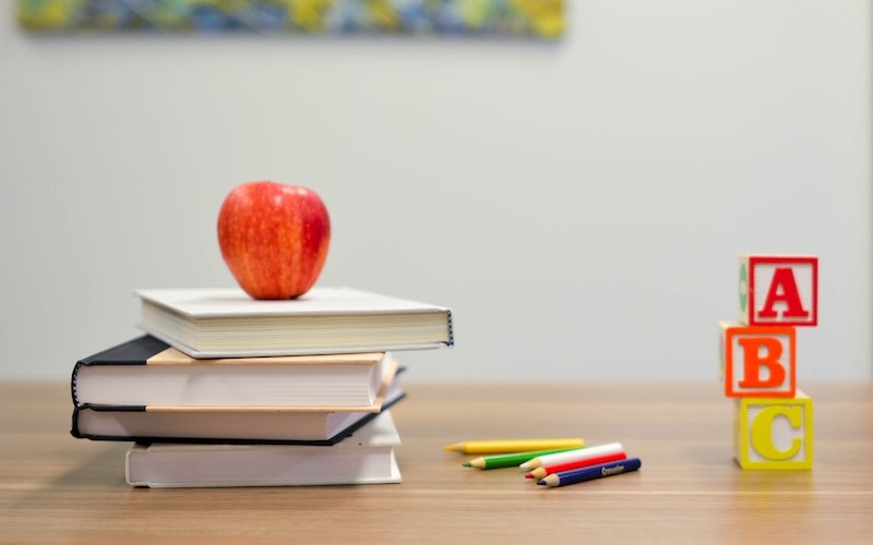 colorful ABC blocks, books, coloring pencils and a red apple are arranged on a wooden table