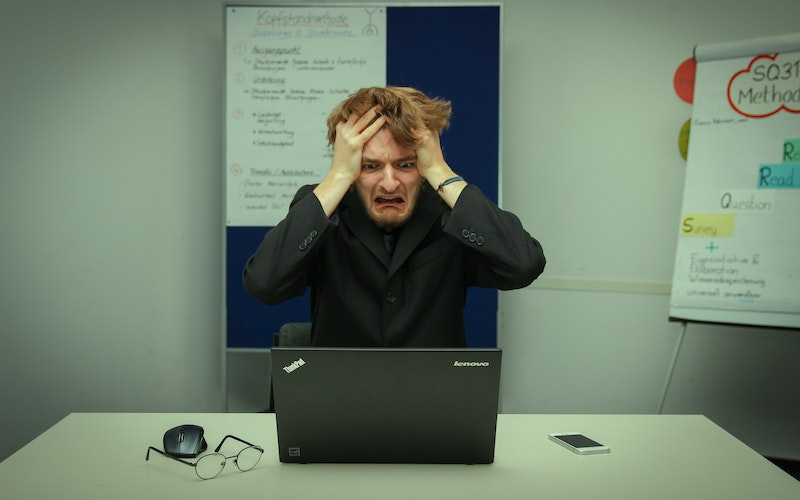 a frustrated young male adult holding his head with both hands staring at a laptop