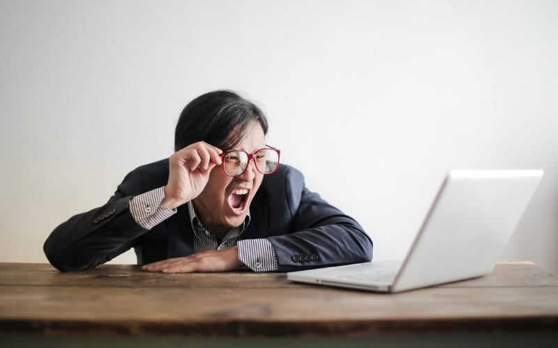 a shocked man holding his red glasses while staring at his white laptop screen