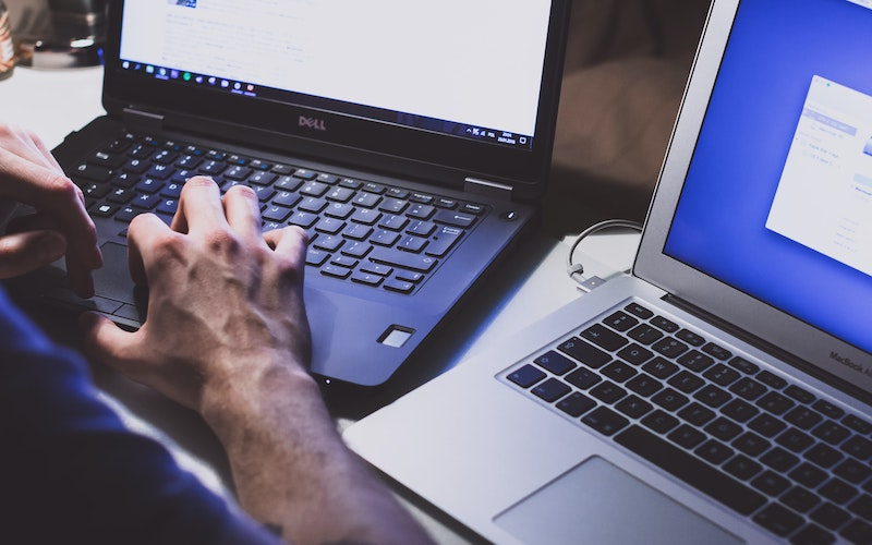 a dell laptop being used beside a macbook air laptop both turned on
