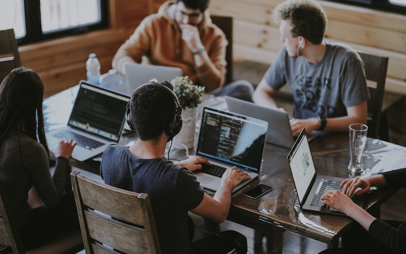 a workspace with young adults using laptops collaborating, listening to audio and typing