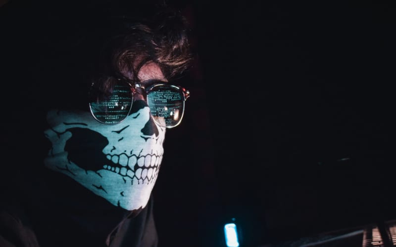 a close up view of a man wearing a skull bandana with a reflection of computer data in his eyeglasses