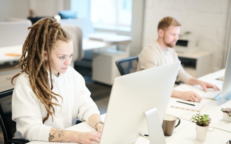 a man and woman with dreadlocks focused on their computers in a collaborative workspace
