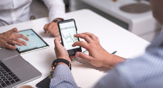 business individuals seated at a table, actively using smartphones to view graph and data