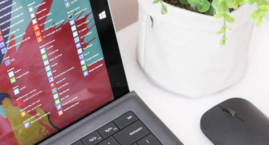 a cropped image of a laptop displaying microsoft 365 applications beside a wireless mouse and a pot with plant