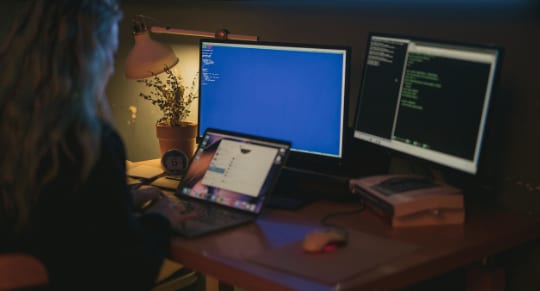 a woman working on her laptop with two computer screens turned on simultaneously